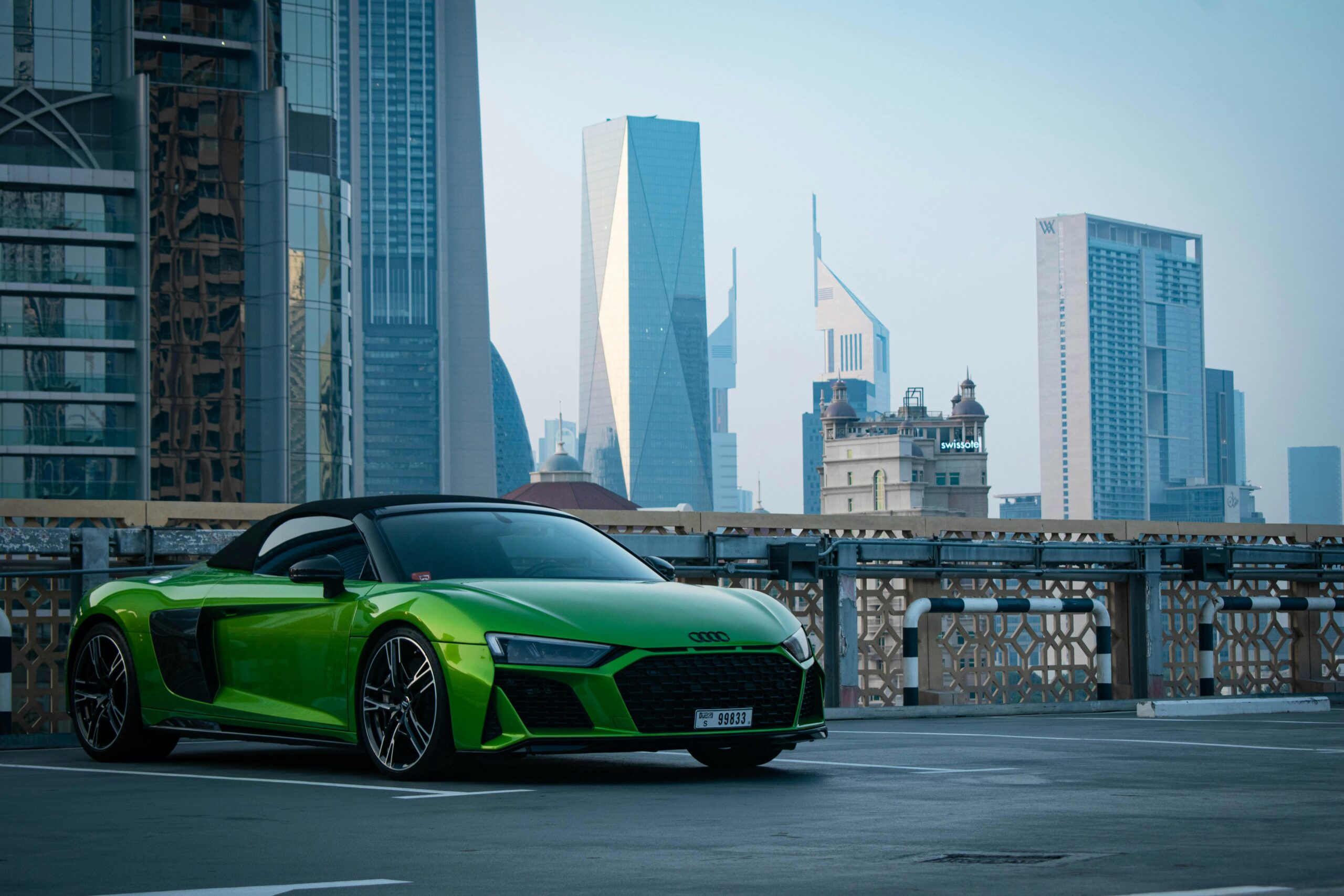 A vibrant green Audi R8 parked against Dubai's iconic skyscrapers, showcasing urban luxury.